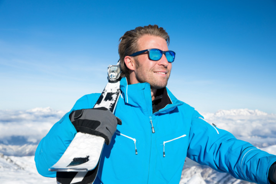 Man holding skis looking into the distance through his polarised UV protective sunglasses