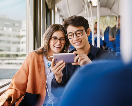 Woman and man sat on bus looking at smartphone