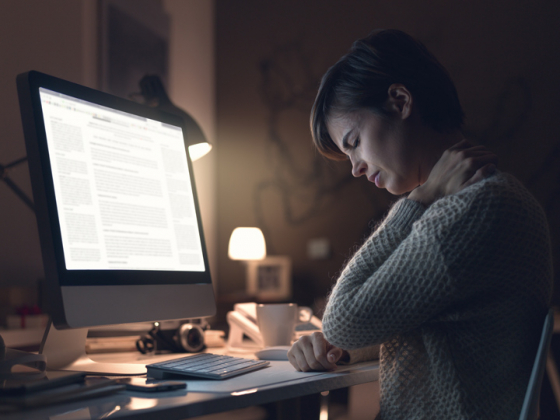 Woman holding neck in pain whilst working on bright computer screen