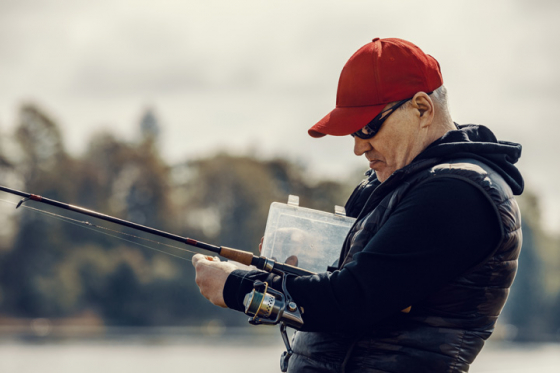 Man wearing sunglasses tying hook on fishing line
